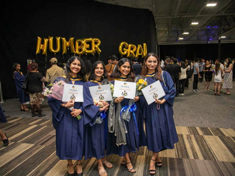Four graduates holding their certificates smile for camera