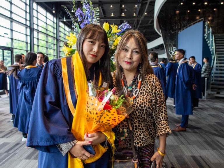 Graduate holding flowers poses for photo with her mother