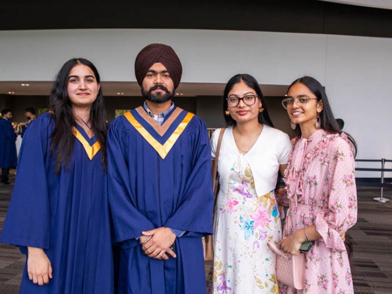 Two graduates pose for photo with two ceremony guests