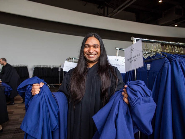 Person in black gown holds blue gowns on their arms