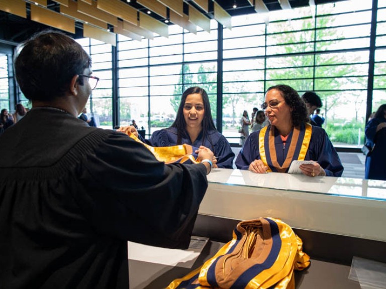 Two graduates receive their sashes over counter
