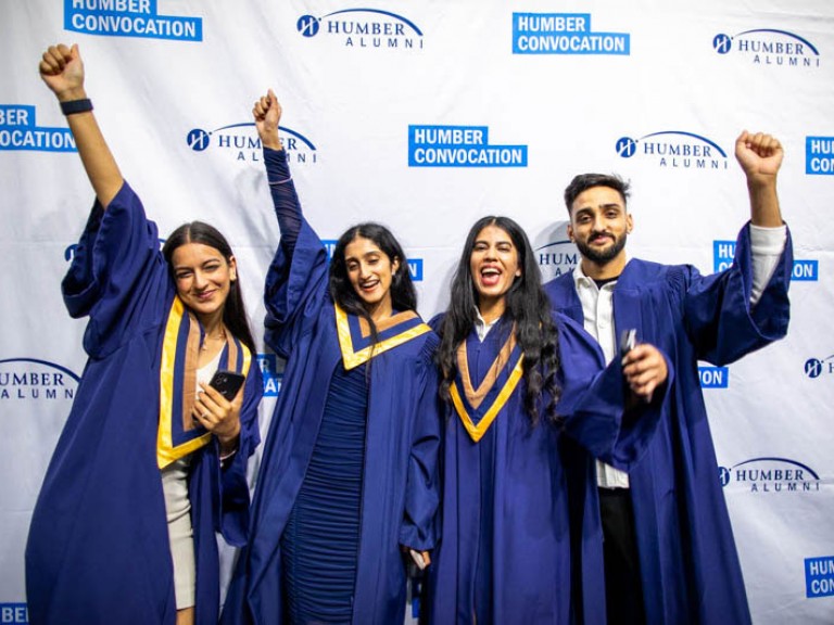 Four graduates raise hands in excitement