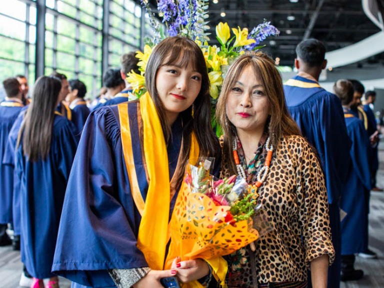 Graduate holding flowers takes photo with her mom