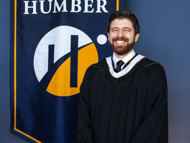 Honorary degree recipient Tareq Hadhad smiles for photo in front of Humber flag
