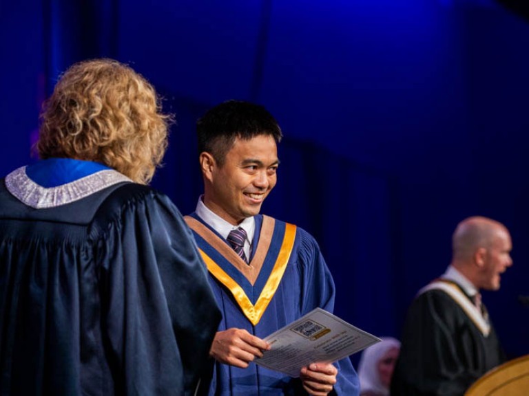 Graduate smiles towards audience with their certificate in hand