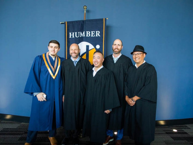 Five people stand together in front of Humber flag