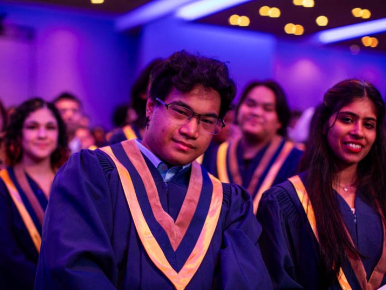 Graduate sitting in ceremony audience looks at camera