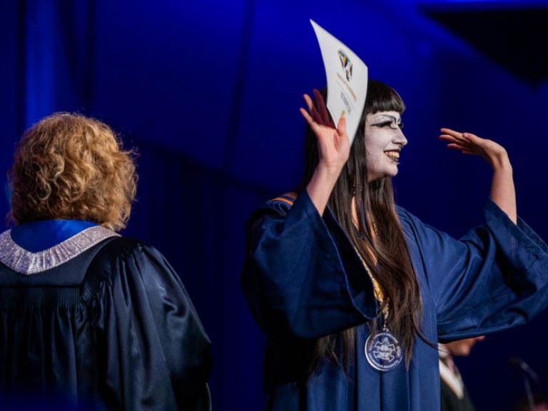 Graduate smiles at the audience with hands raised