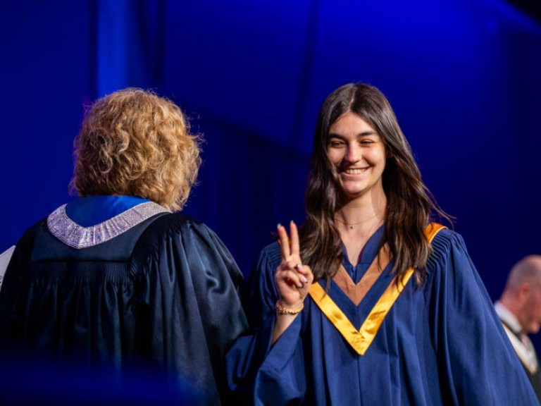 Graduate smiles and holds up a peace sign