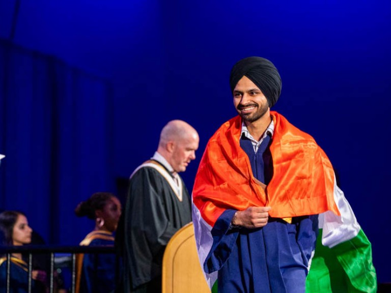 Graduate crosses stage wearing a flag over their shoulders