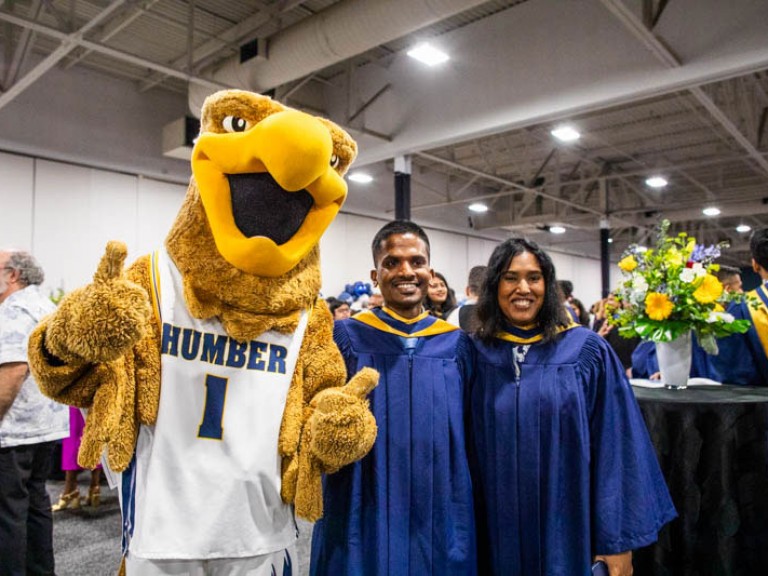 Two graduates take photo with Humber mascot