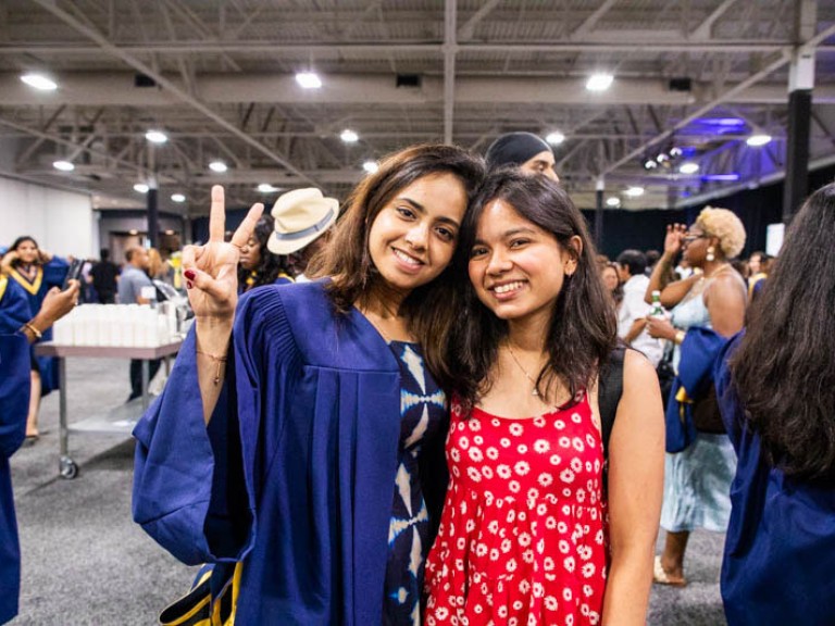 Graduate holds up peace sign as they pose for photo with guest