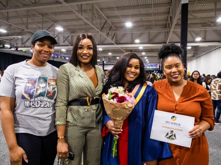 Graduate holding flowers poses with three guests