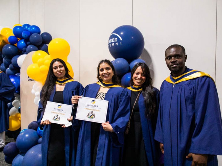 Four graduates pose for photo in front of balloons