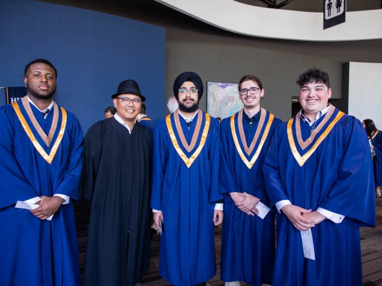 Four graduates pose with another for photo