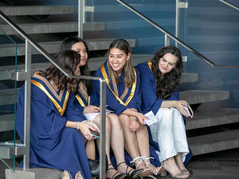 Four graduates sitting on steps talking