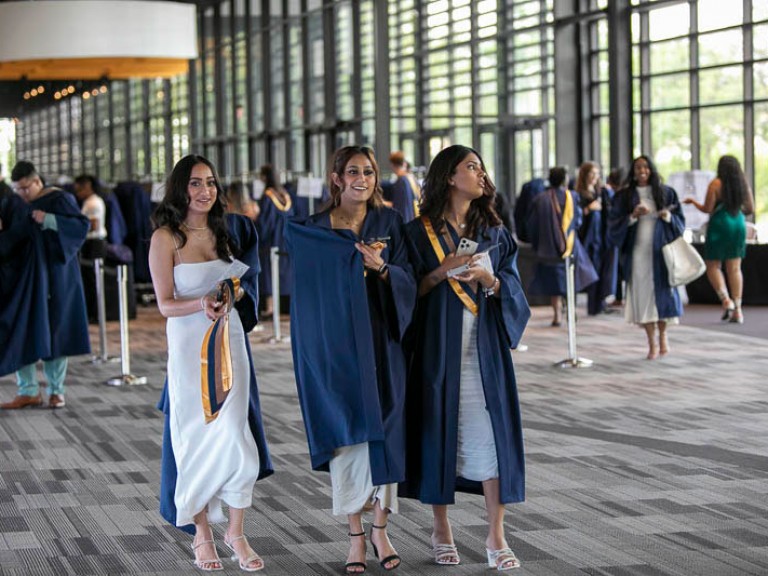 Three graduates putting robes on