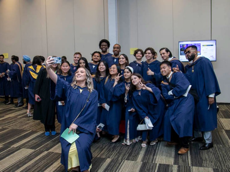 Graduate takes a selfie with a large group of graduates behind her
