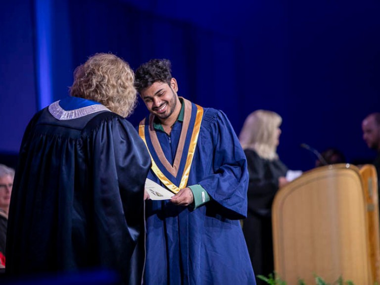 Graduate smiles as they receive certificate