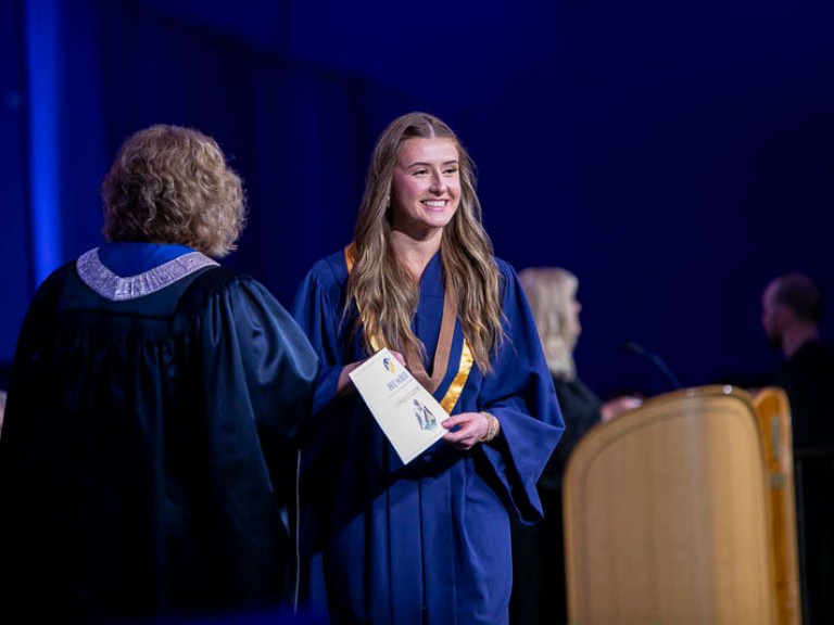 Graduate smiles towards audience with their credential