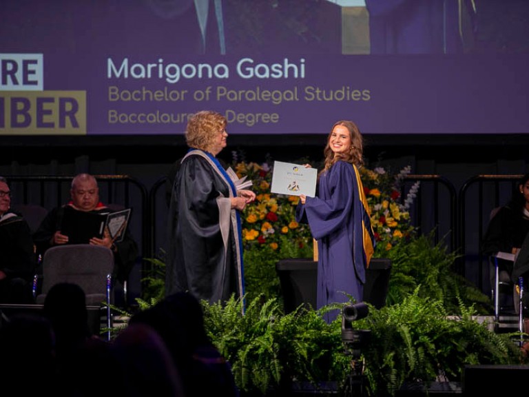Graduate Marigona Gashi on stage with her name on screen