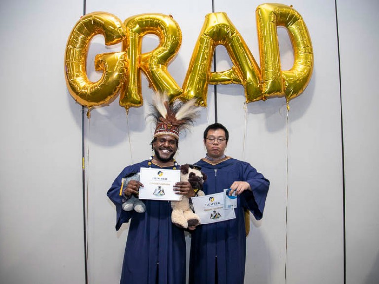 Two graduates take photo beneath GRAD balloons