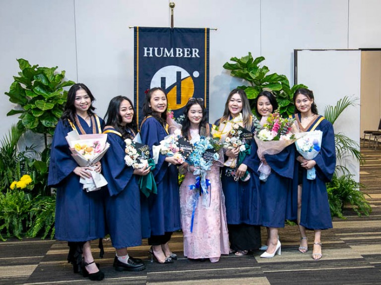 Seven graduates holding flowers pose for photo