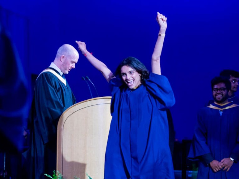 Graduate raises both arms as they cross ceremony stage