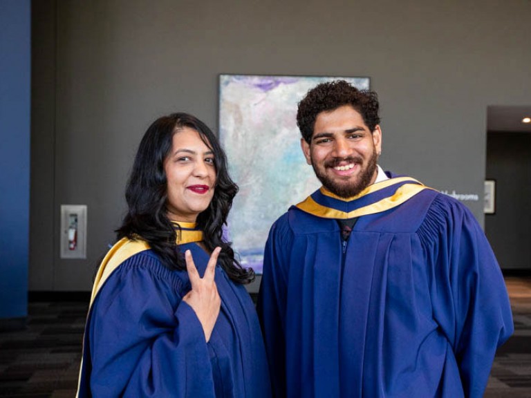 Two graduates pose for photo, one holds up a peace sign