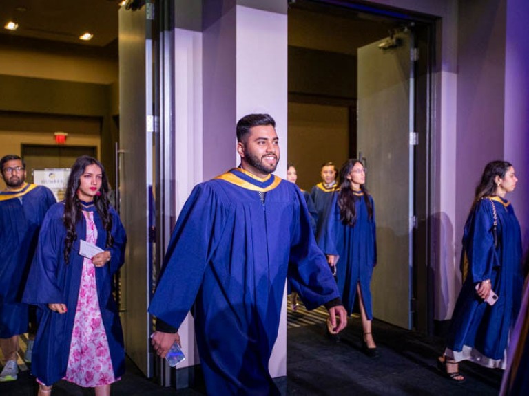 Two lines of Humber graduates enter through doorway