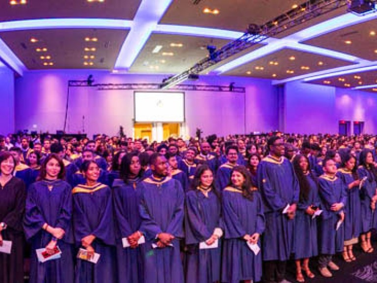 Wide shot of ceremony hall filled with standing graduates