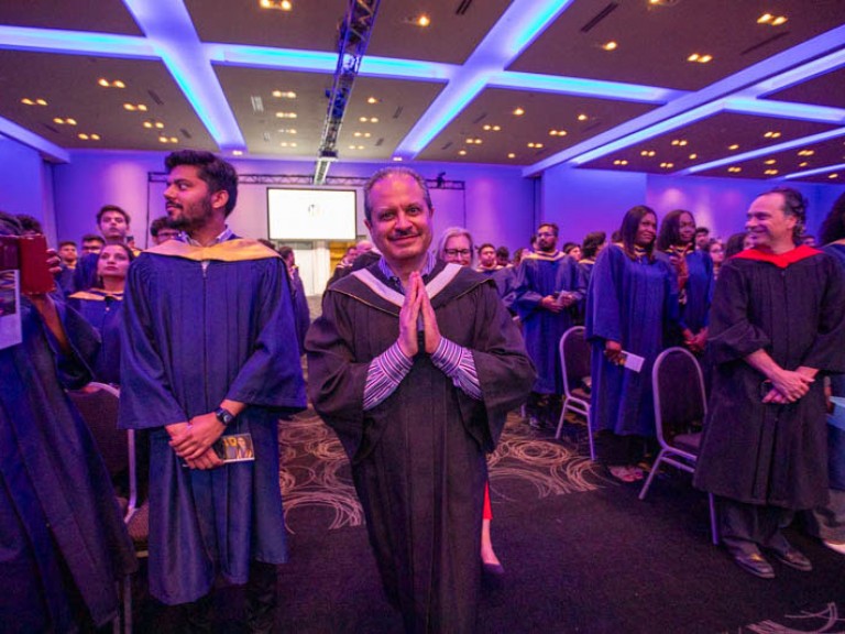 Faculty member makes prayer hands as they walk past camera