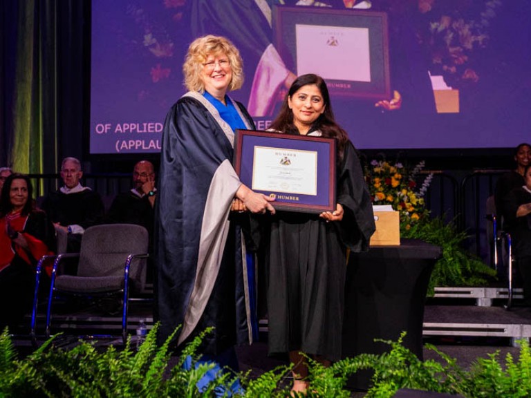 Honorary degree recipient Deepa Mattoo holding framed award with Humber president on stage