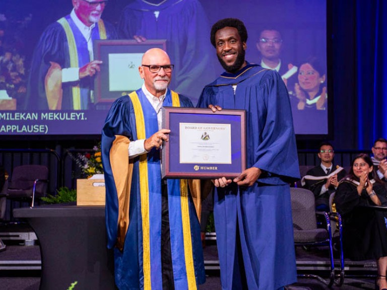 Graduate and faculty member hold framed award on stage