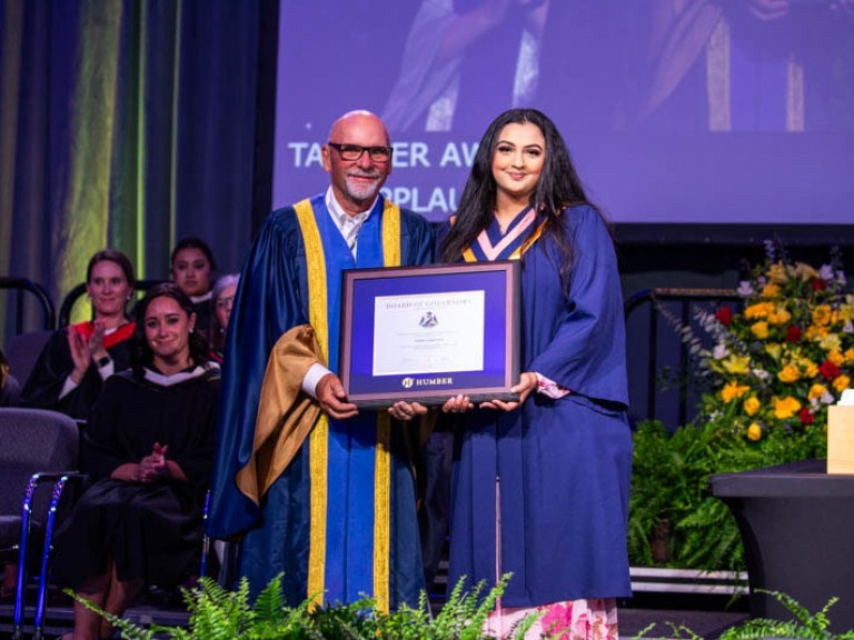 Graduate on stage holding framed award with faculty member