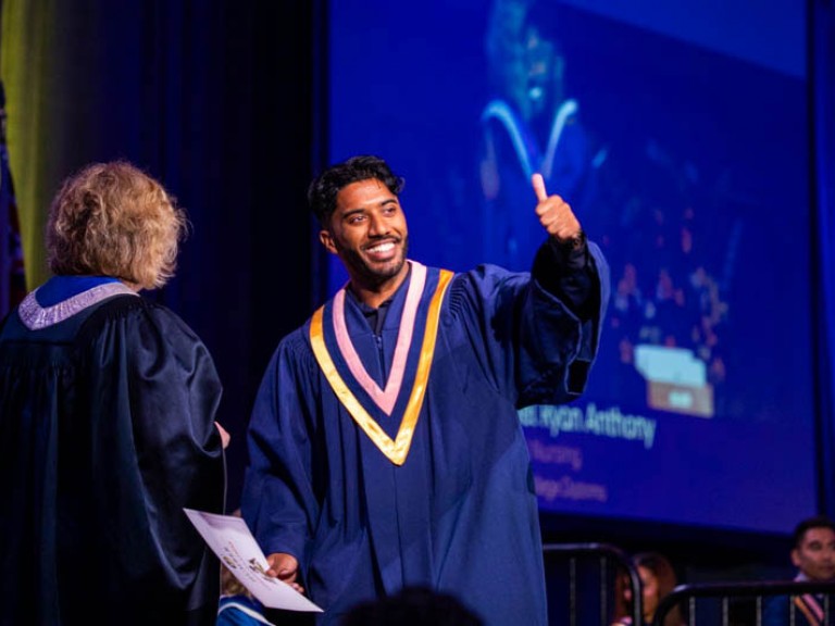 Graduate makes thumbs up as they leave the ceremony stage