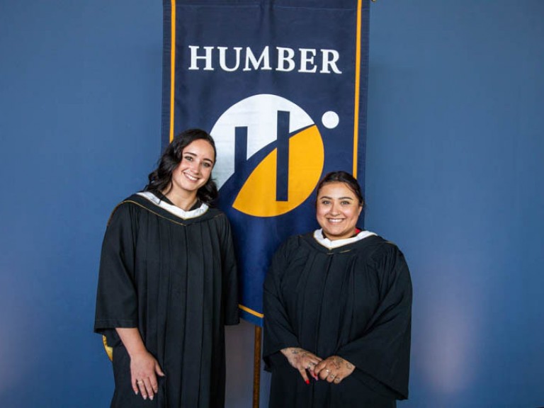 Honorary degree recipient Kaetlyn Osmond poses with another person in front of Humber flag