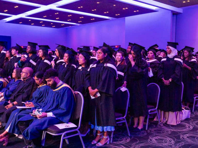 Group of graduates in black gowns and caps standing in the audience