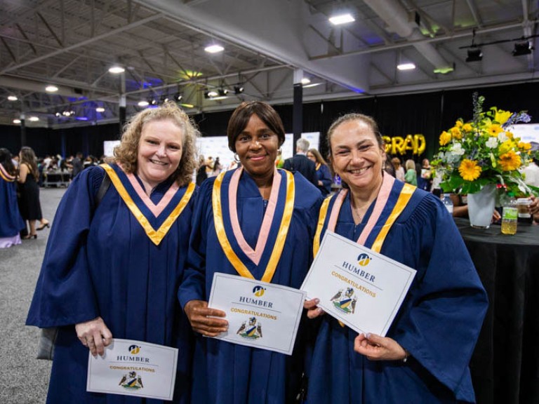 Three graduates holding their certificates pose for camera