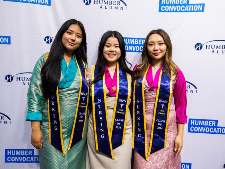 Three Bachelor of Nursing graduates wearing sashes smile for camera