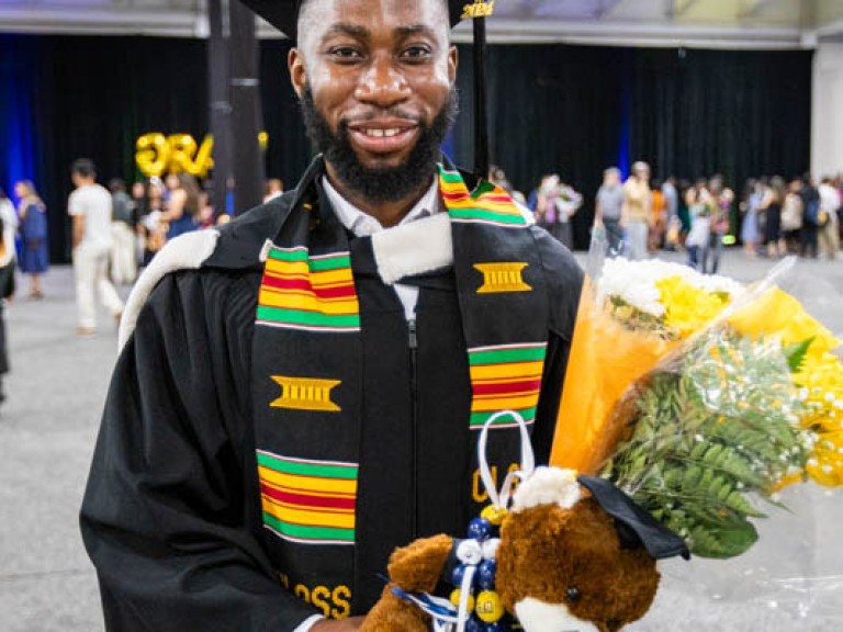 Graduate holding teddy bear and flowers smiles for camera