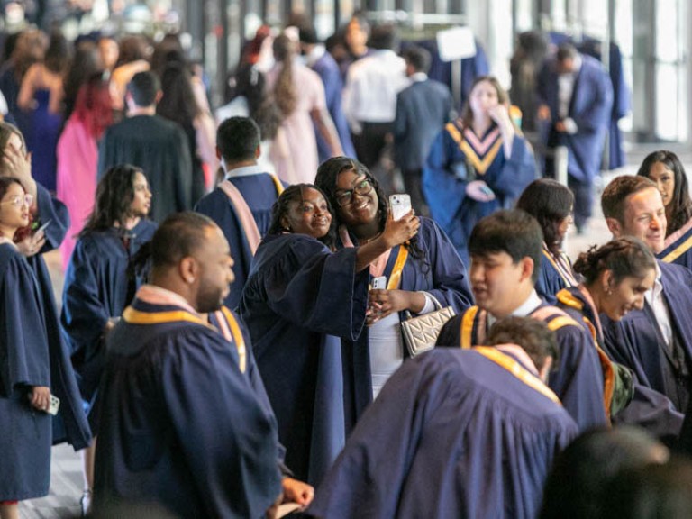 Two graduates take a selfie together among the crowd of graduates