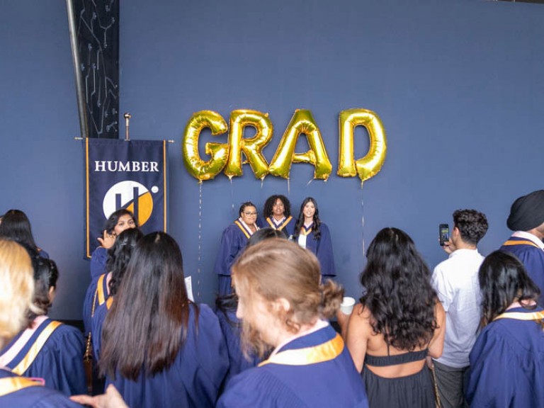 Three graduates standing under GRAD balloons getting their photo taken