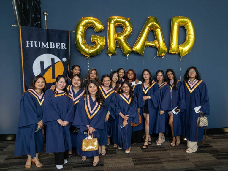Group of graduates pose for photo beneath GRAD balloons