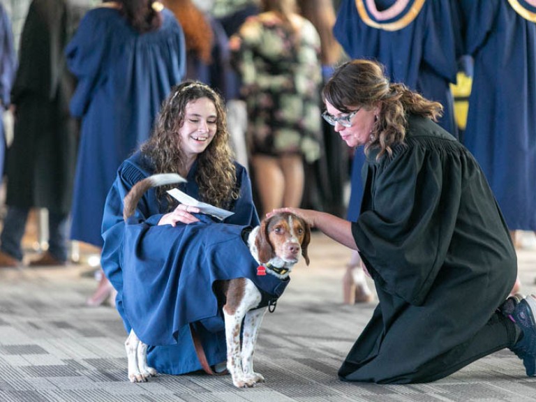 Person petting a graduate's dog wearing a gown
