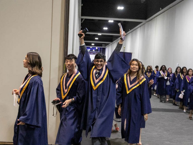 Graduate raises arms as they proceed in line out of hallway