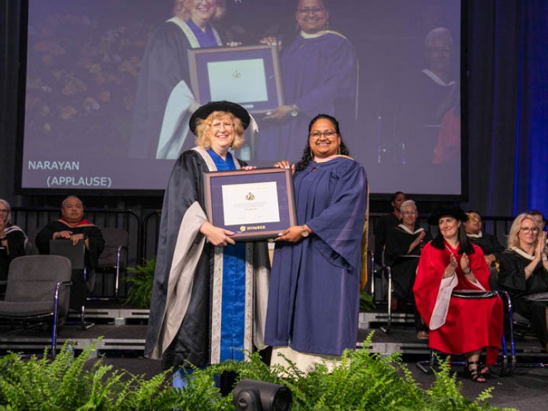 Graduate and Humber president hold a framed award on stage