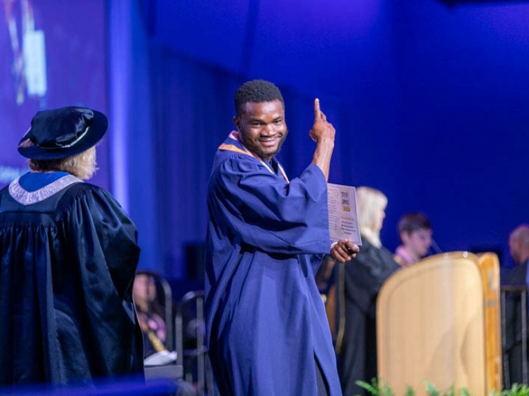 Graduate on stage smiling with arm raised
