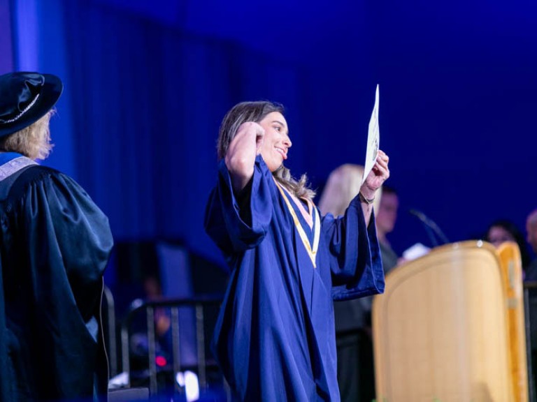 Graduate holds certificate with their tongue out