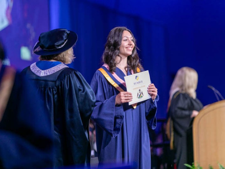 Graduate smiles towards audience with their certificate